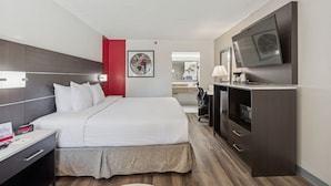 A hotel room with a bed, a desk, a TV, and a mirror. - Ramada by Wyndham Temple Terrace/Tampa North (Tampa)