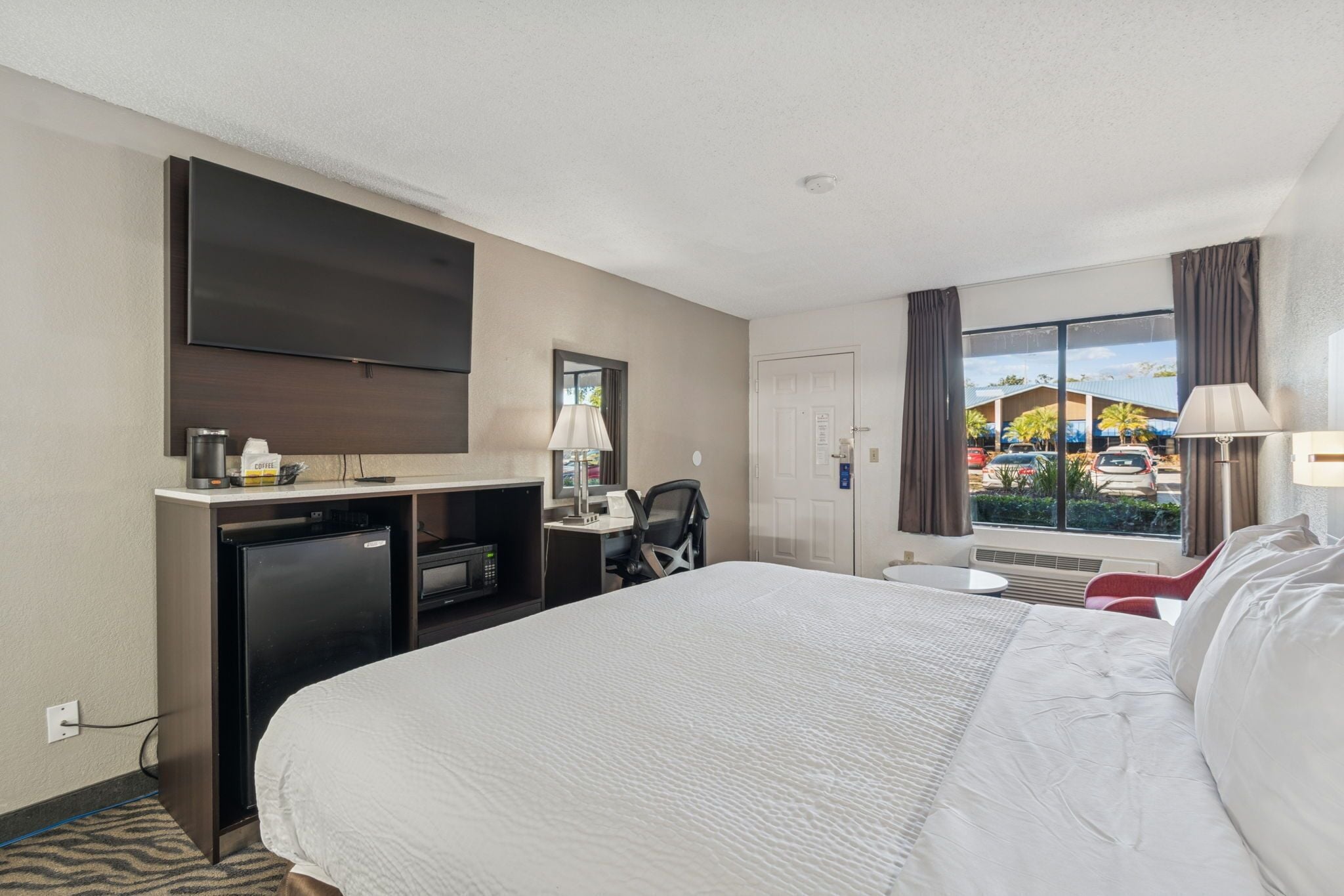 Habitación de hotel con una cama grande, un escritorio con computadora, televisión y ventana con vista al exterior.