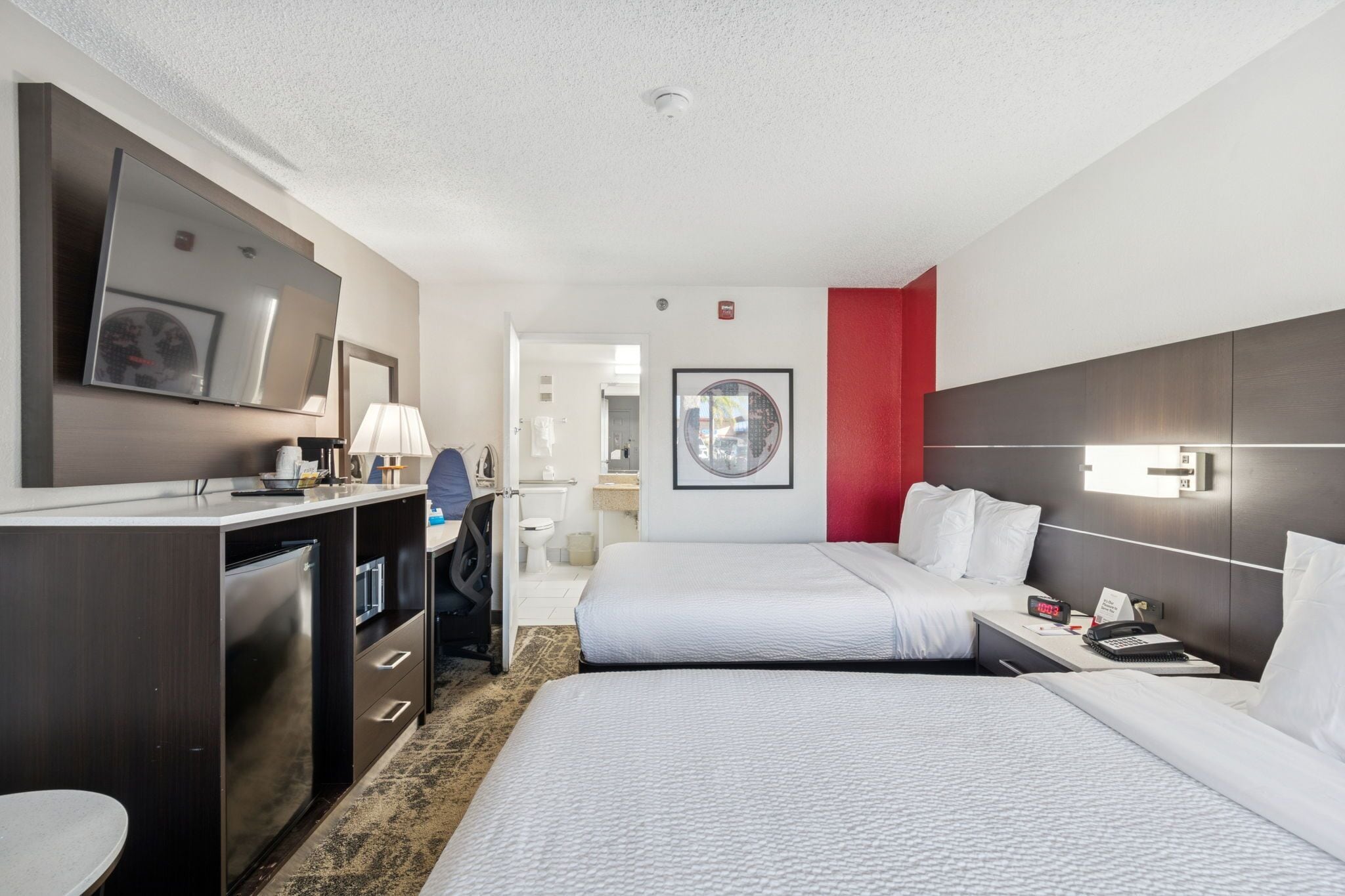 A hotel room with a bed, bedside table, lamp, and a large mirror.