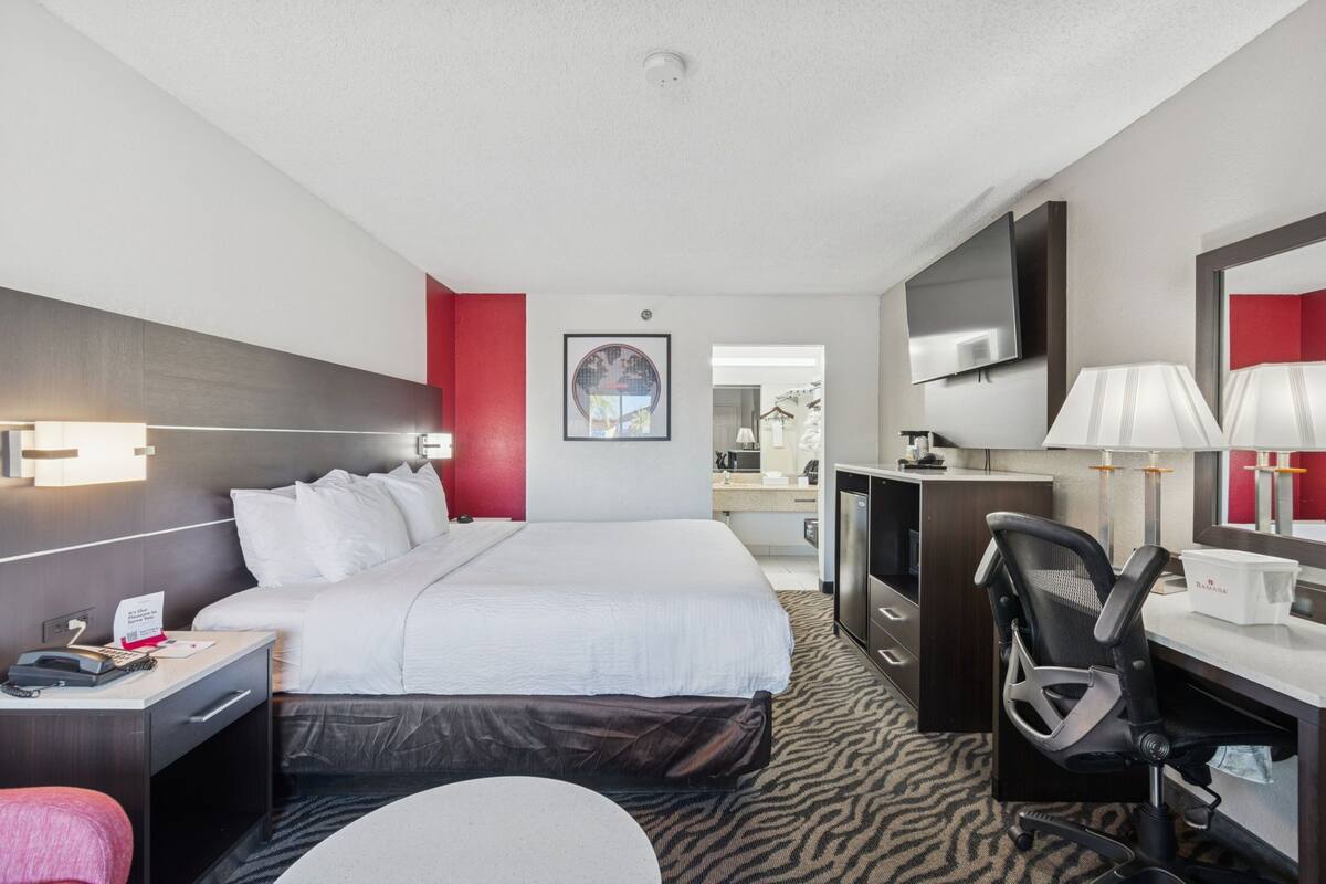 A hotel room with a bed, desk, chair, TV, and a bathroom visible in the background.