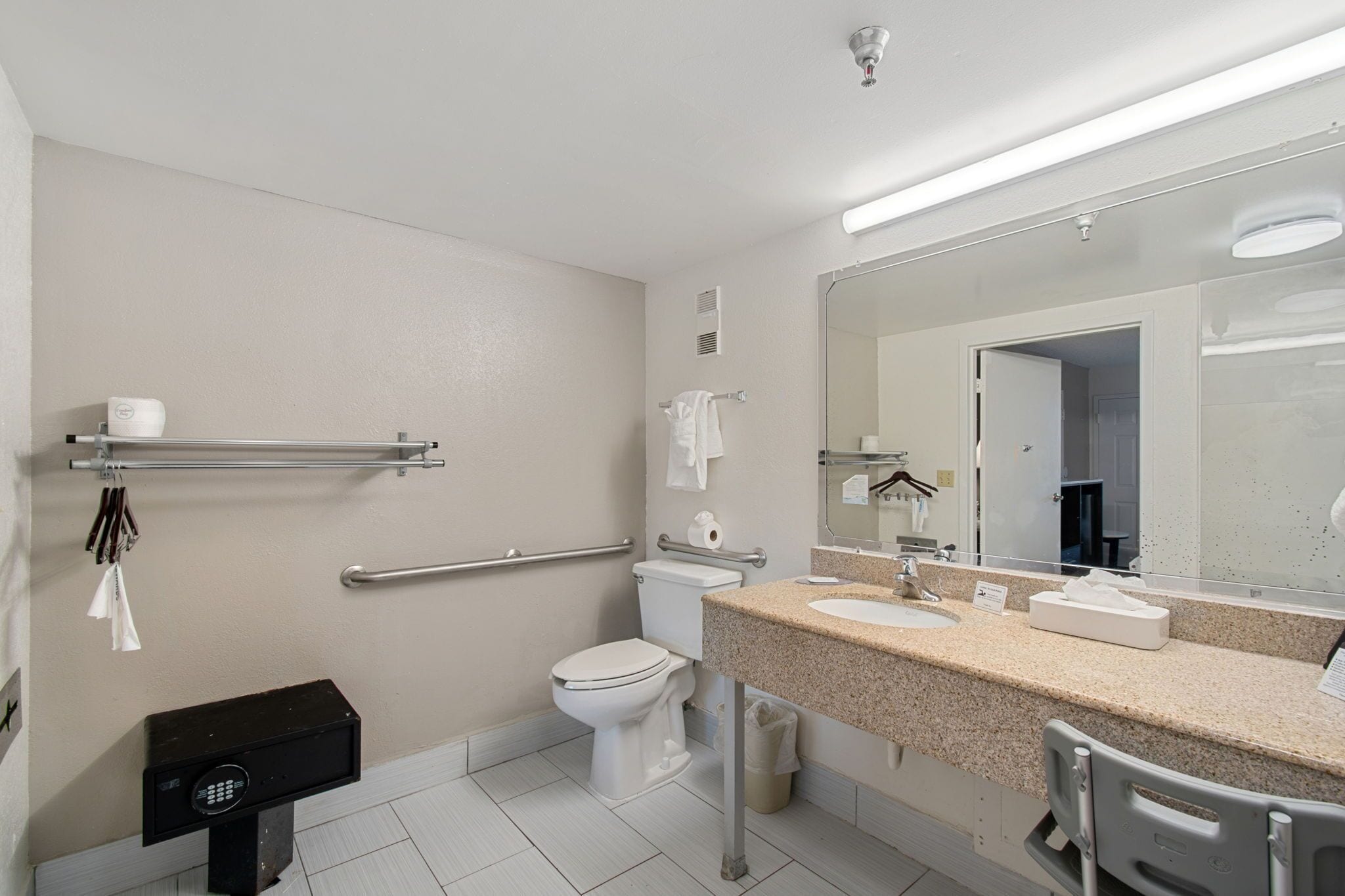 A modern bathroom with a toilet, bidet, hand dryer, towel rack, and a large mirror.