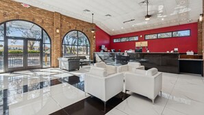 A modern lobby with a glass door entrance, a reception desk, white sofas, and a red accent wall. - Ramada by Wyndham Temple Terrace/Tampa North (Tampa)