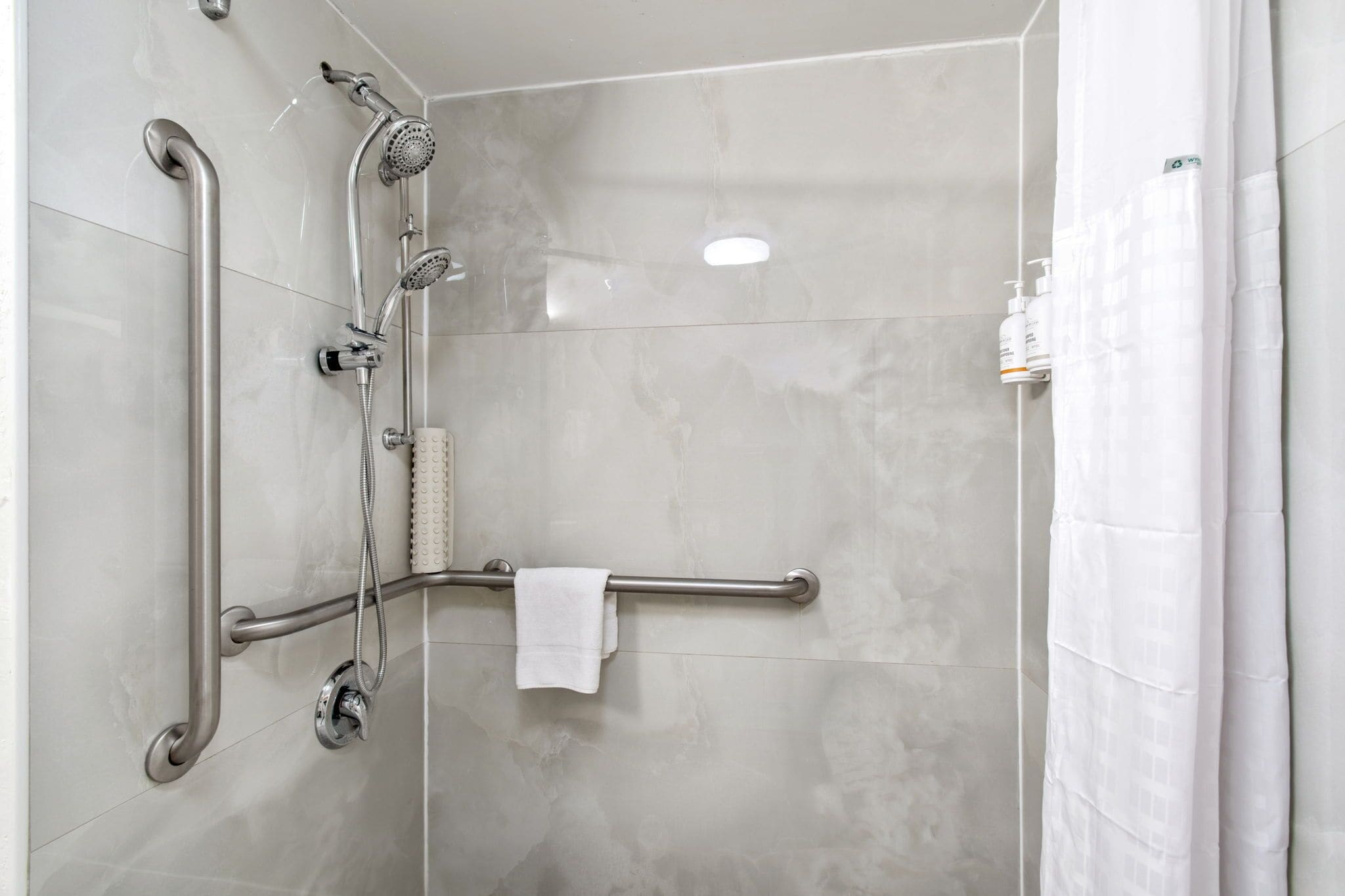 A shower area with a grab bar, handheld showerhead, and a towel rack.