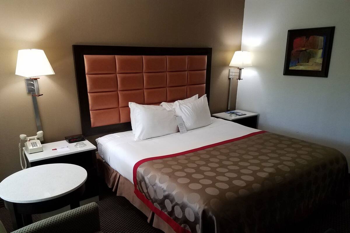A hotel room with a bed, two bedside tables, a round table, a telephone, and a painting on the wall.