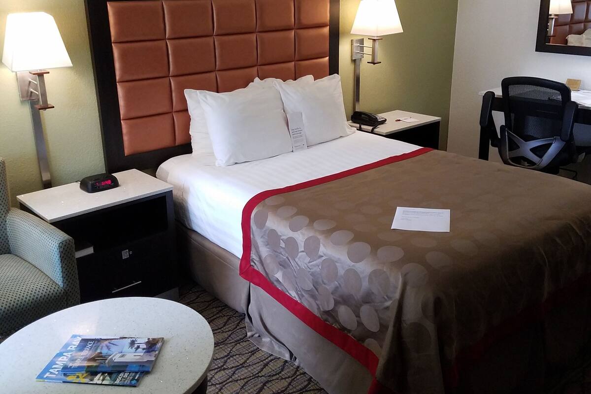 A hotel room with a bed, two bedside tables, a chair, a small round table, and a desk with a chair.