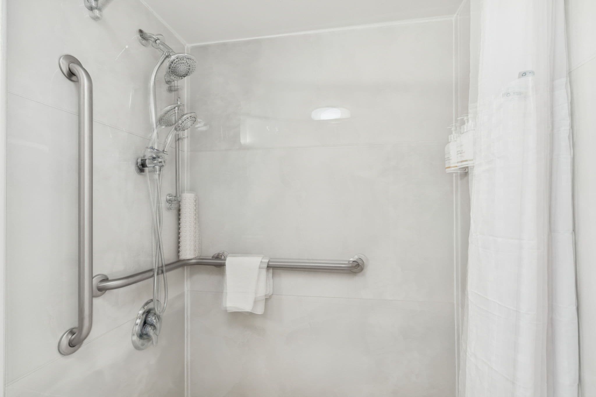 A modern shower with a handheld showerhead, a handheld shower attachment, and a handheld shower control.