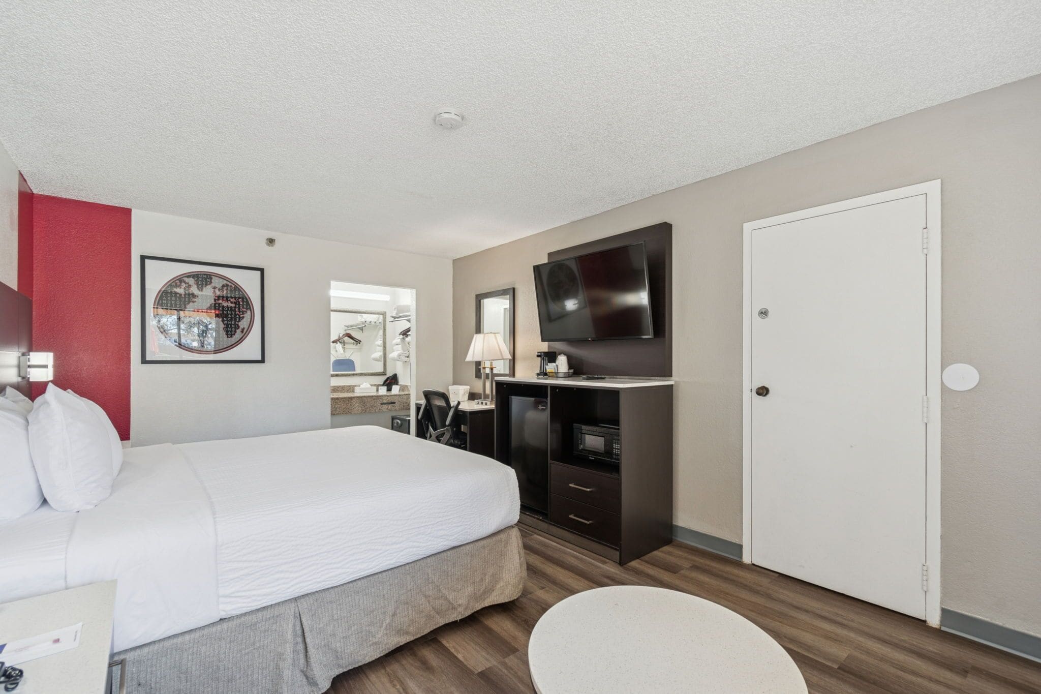 A hotel room with a bed, a desk with a TV, a microwave, and a wardrobe.