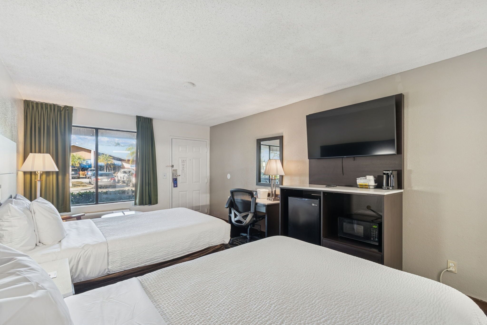 A hotel room with two beds, a desk with a computer, a TV, and a window with curtains.