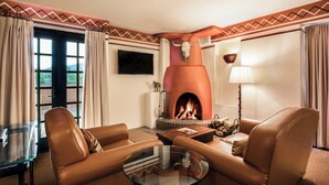 A living room with leather sofas, a glass coffee table, a fireplace with a bull skull decoration, a flat-screen TV, and a lamp.