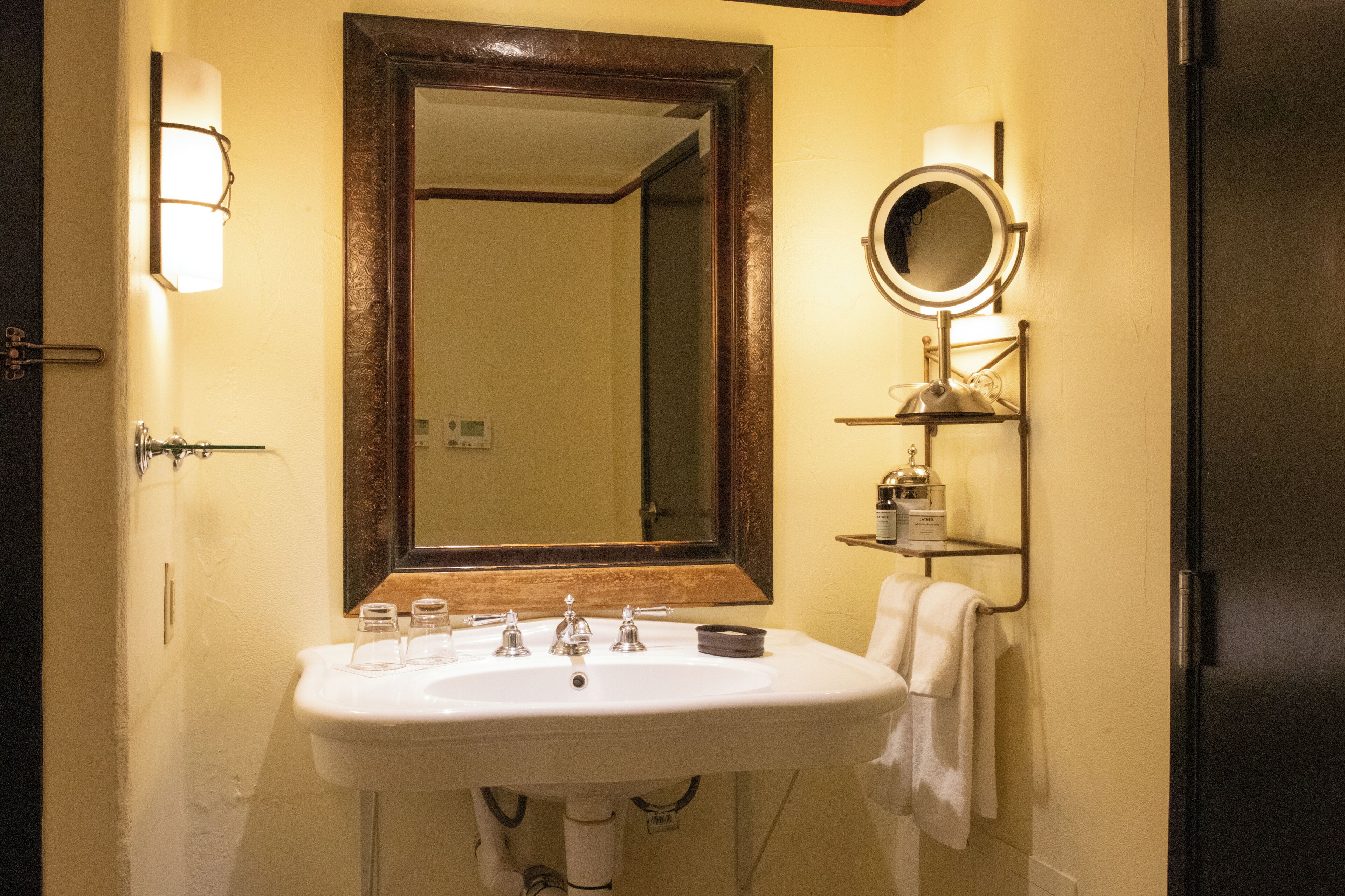 A bathroom with a white sink, a mirror with a wooden frame, a towel rack, and a shelf with toiletries.