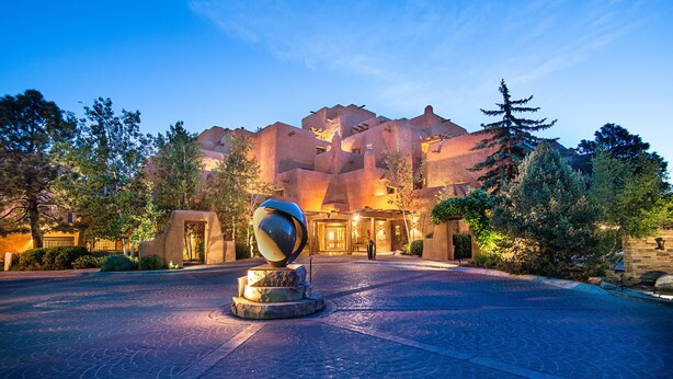 A hotel entrance with a unique architectural design, a central sculpture, and a paved courtyard.