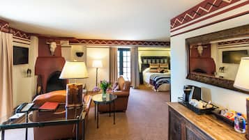 Une chambre d’hôtel équipée d’un canapé, d’un fauteuil, d’une table, d’une lampe, d’une cheminée et d’un miroir.