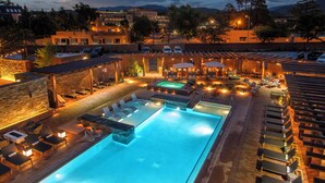 A swimming pool with lounge chairs and umbrellas, surrounded by buildings and trees.