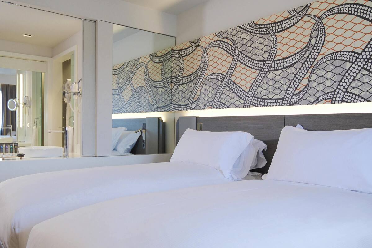 A modern hotel room with a large bed, a bathroom with a mirror, and a decorative wall pattern.