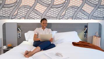 Una persona sentada en una cama con una tableta, una revista y una chaqueta marrón sobre la cama.