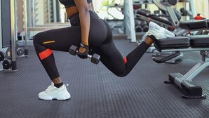 Un gimnasio con equipamiento de ejercicio, una persona realizando un ejercicio para piernas, y un techo con luces.
