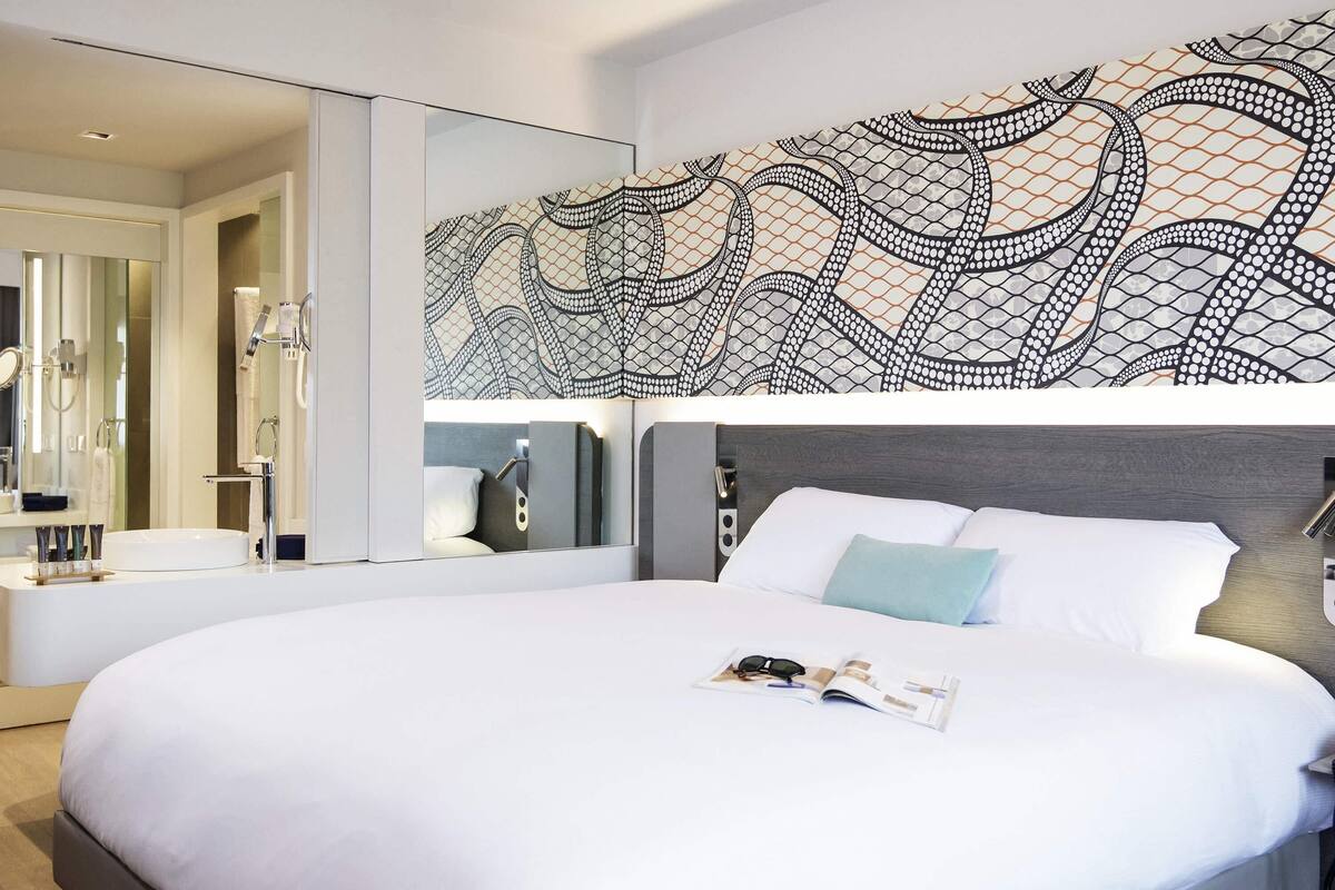 A modern hotel room with a large bed, a built-in vanity with a mirror, and a decorative wall pattern.