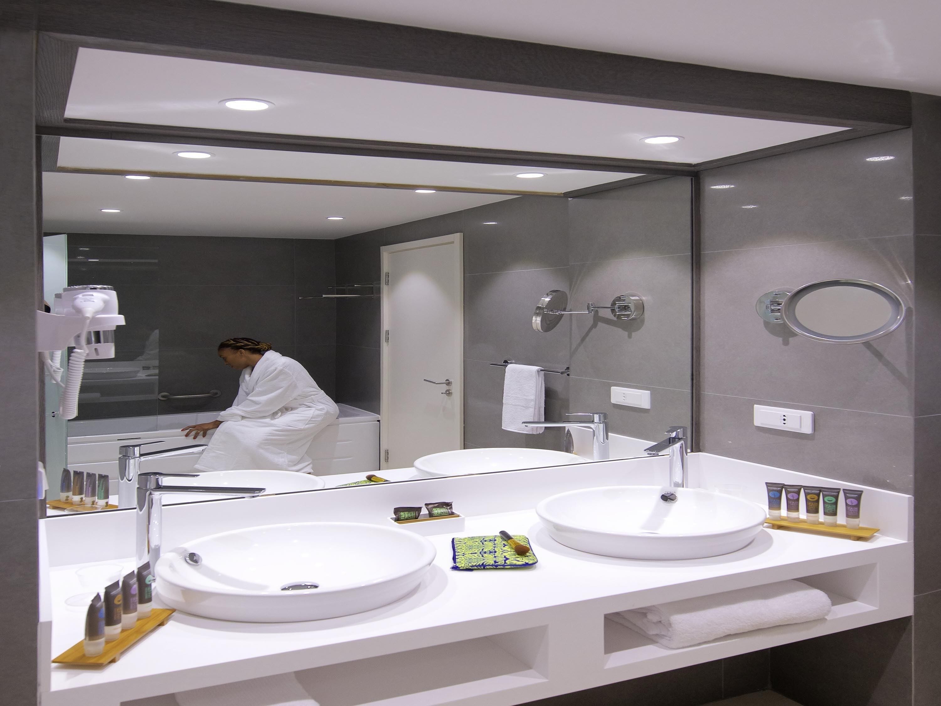 A modern bathroom with two sinks, a large mirror, and a hairdryer.