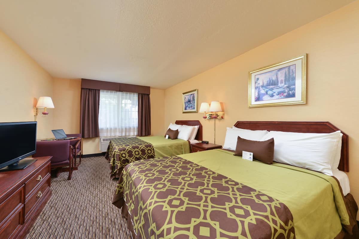 A hotel room with two beds, a TV, a desk, and a window with curtains.
