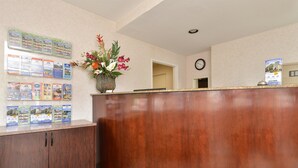 A reception area with a wooden reception desk, a clock on the wall, and a bulletin board with brochures. - Americas Best Value Inn San Jose Convention Center (San Jose)