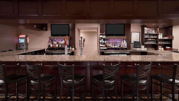 A bar area with a granite countertop, bar stools, and shelves stocked with bottles and glasses.