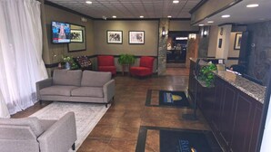 A lobby with a reception desk, red chairs, a grey sofa, and a TV mounted on the wall.