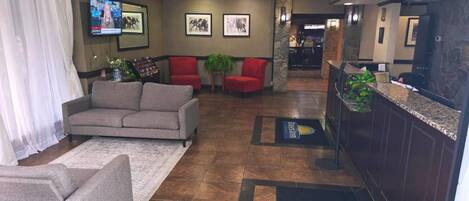 A lobby with a reception desk, red chairs, a grey sofa, and a TV mounted on the wall.