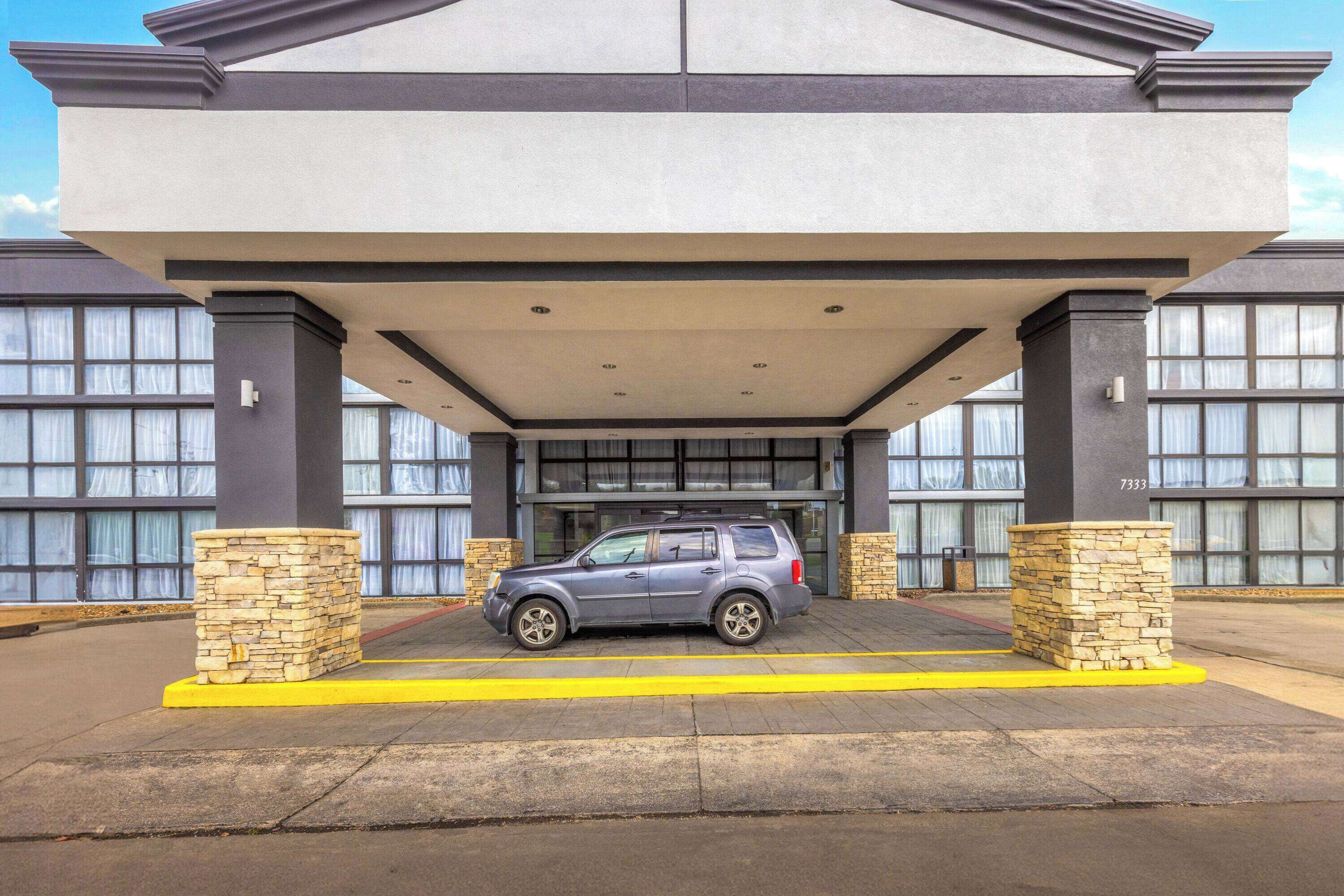A modern building with a covered entrance and a parked SUV.
