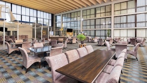 A spacious indoor area with multiple seating arrangements, including tables and chairs, and a large wooden table in the center. - Wingate by Wyndham Kansas City (Kansas City)