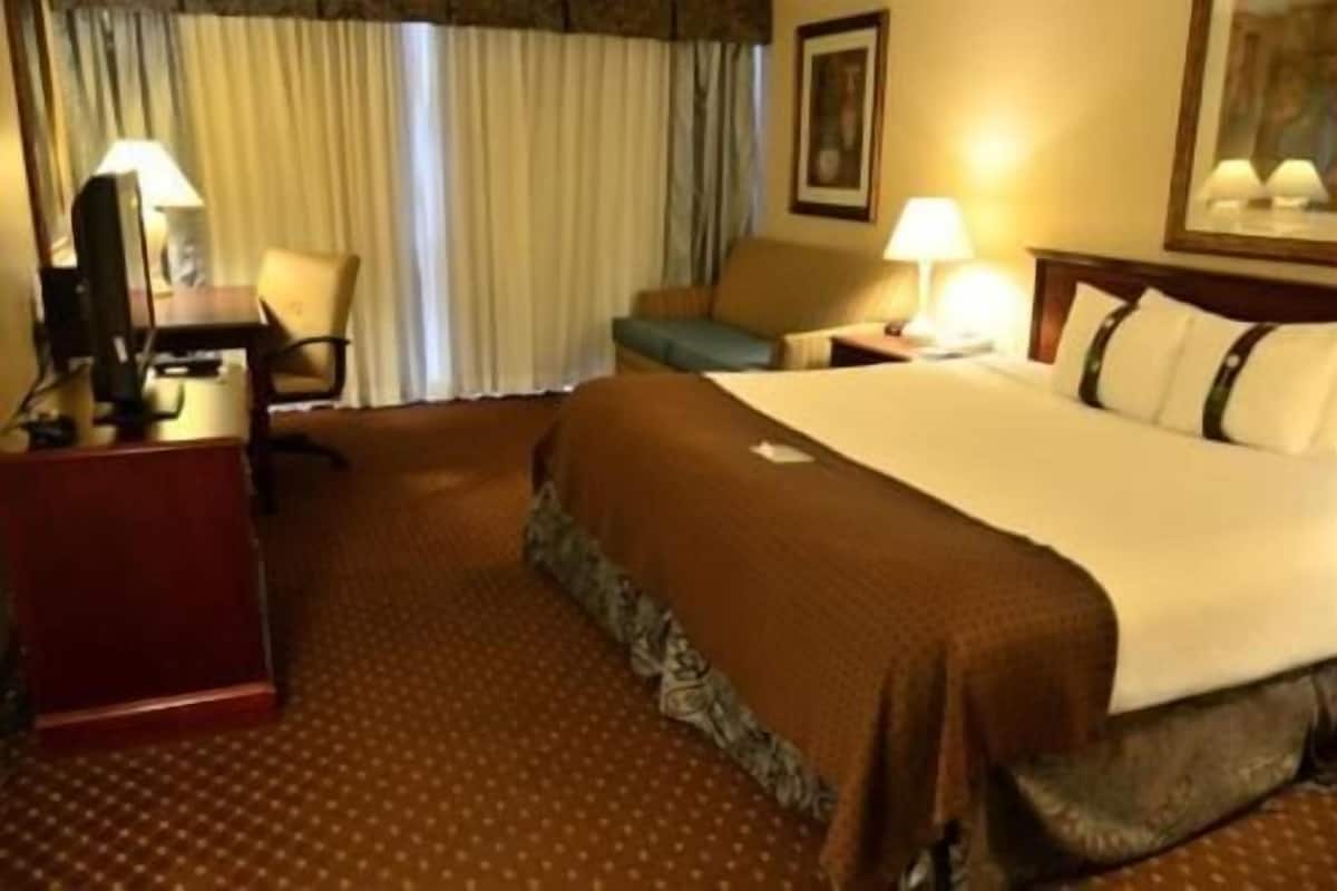 Ein Hotelzimmer mit Bett, Schreibtisch, Stuhl, Lampe und einem Bild an der Wand.