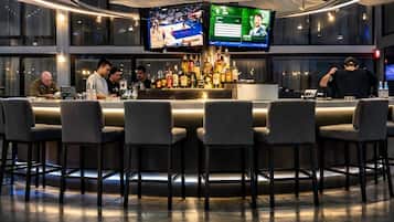 Un bar moderno con varias pantallas, una barra bien surtida y una lámpara circular en el techo.