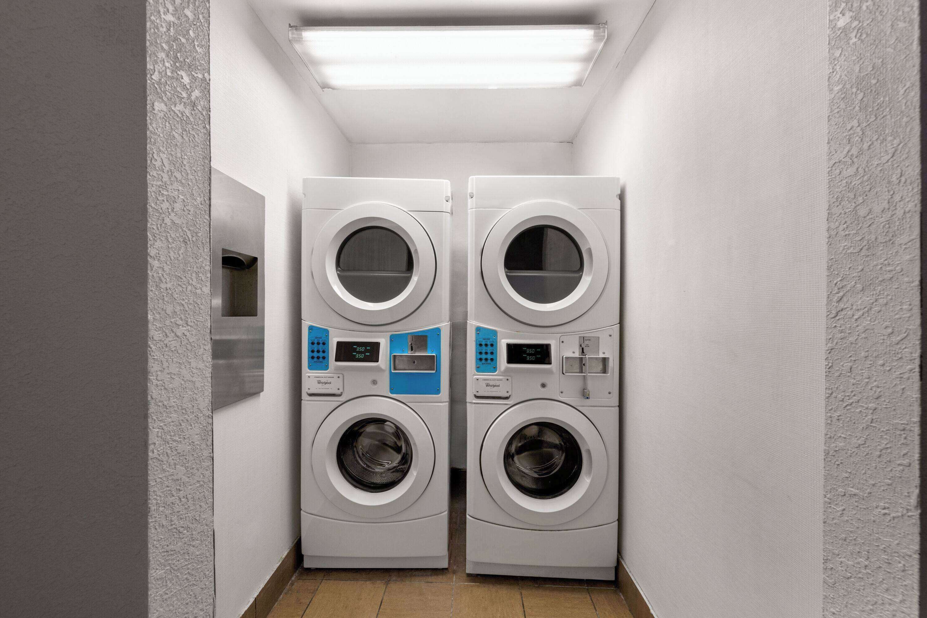A laundry room with two stacked front-loading washing machines and a wall-mounted dryer.