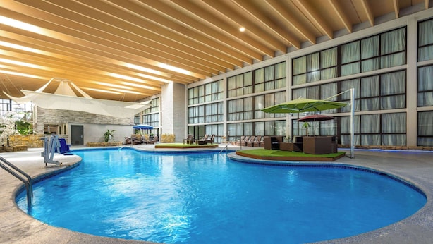 An indoor swimming pool with a wooden ceiling, large windows, and lounge chairs. - Wingate by Wyndham Kansas City (Kansas City)