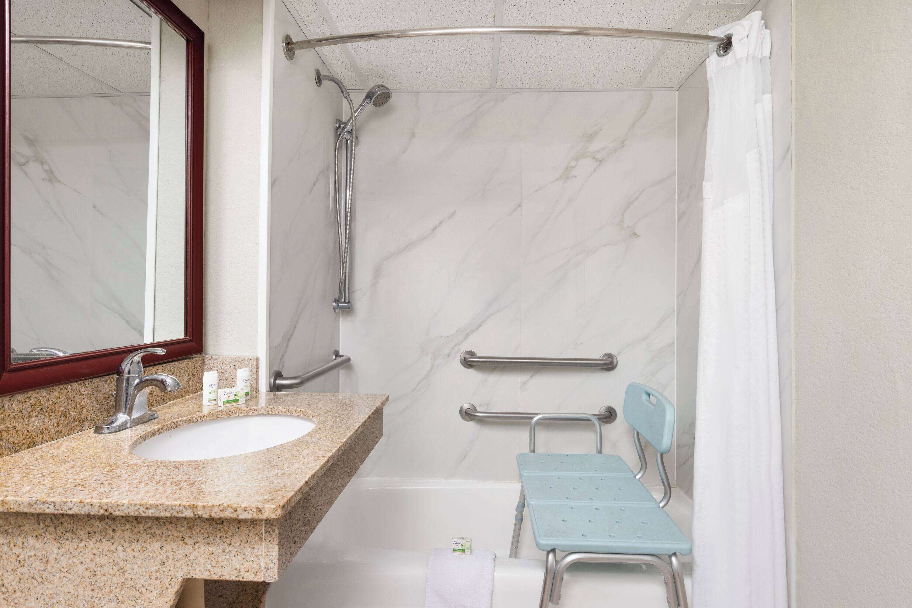 Une salle de bain dotée d’un lavabo en marbre, d’une douche avec une barre d’appui et d’un siège accessible aux personnes en fauteuil roulant.