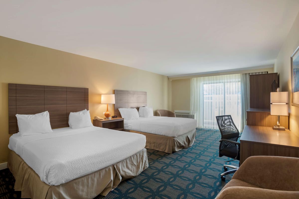 A hotel room with two beds, a desk, a chair, and a large window.