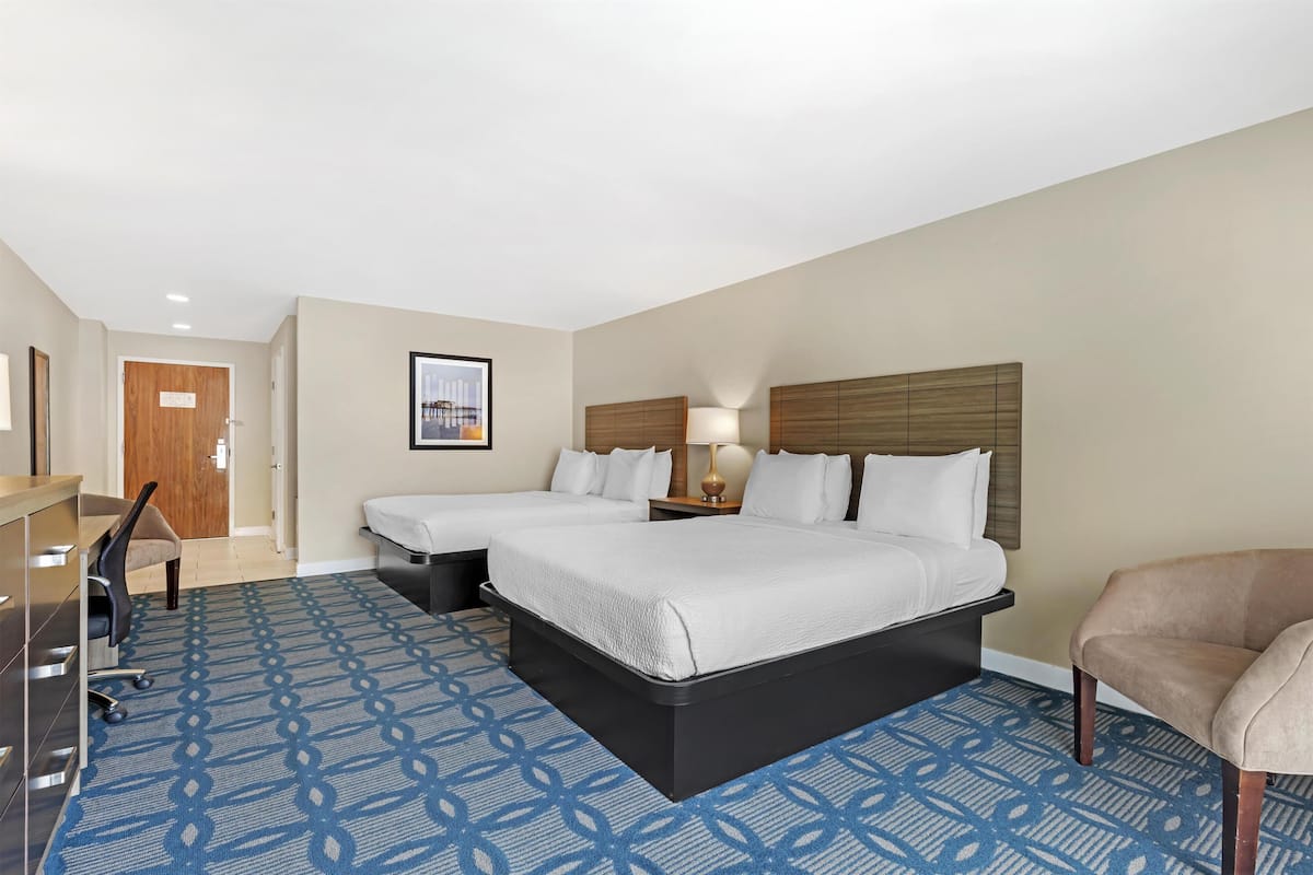 A hotel room with two beds, a desk, a chair, and a patterned carpet.