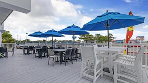 An outdoor patio with tables and chairs, blue umbrellas, and a view of the sea. - Best Western Plus Ocean City (Ocean City)