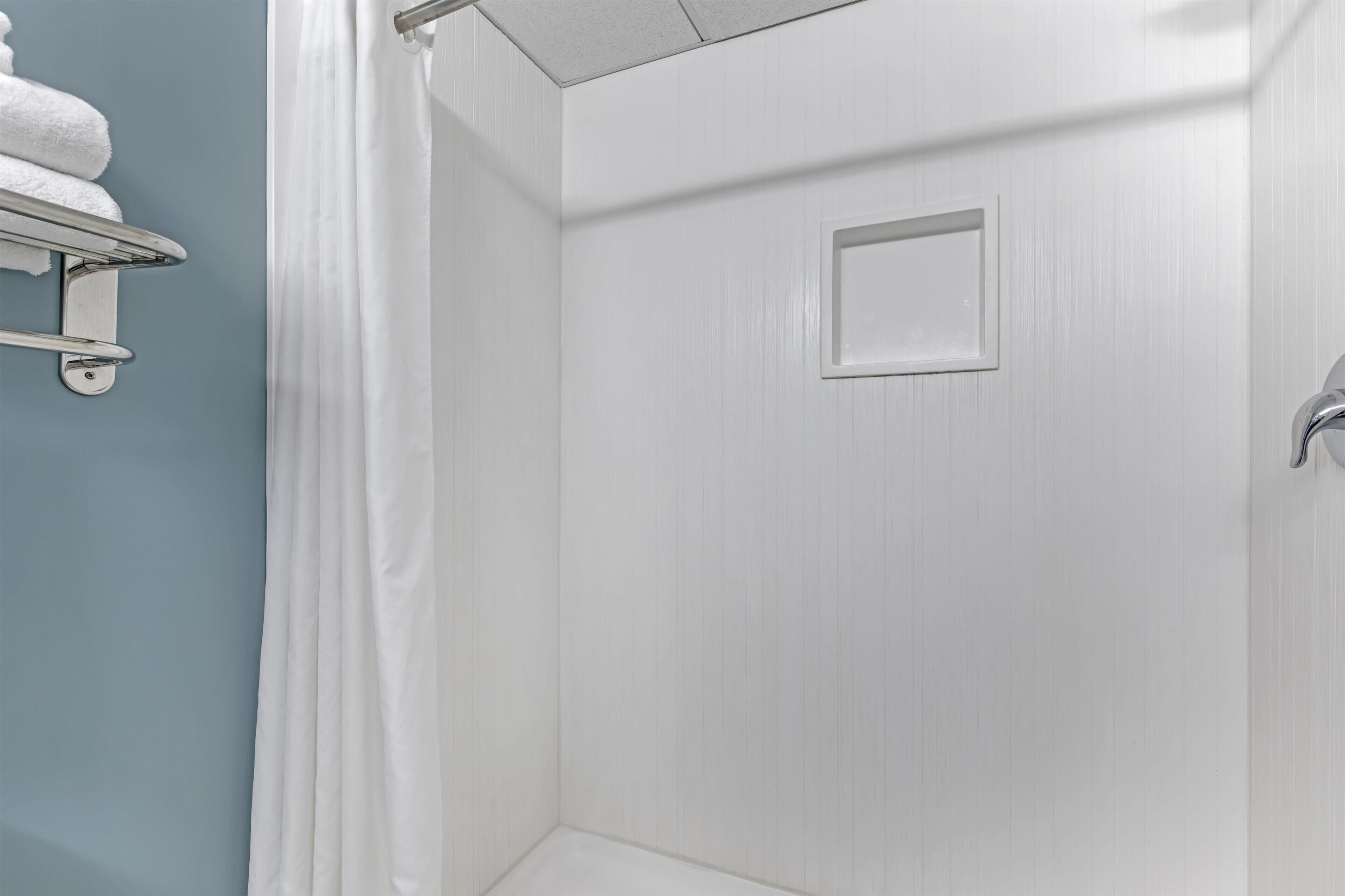 A bathroom with a shower, a towel rack, and a door with a handle.