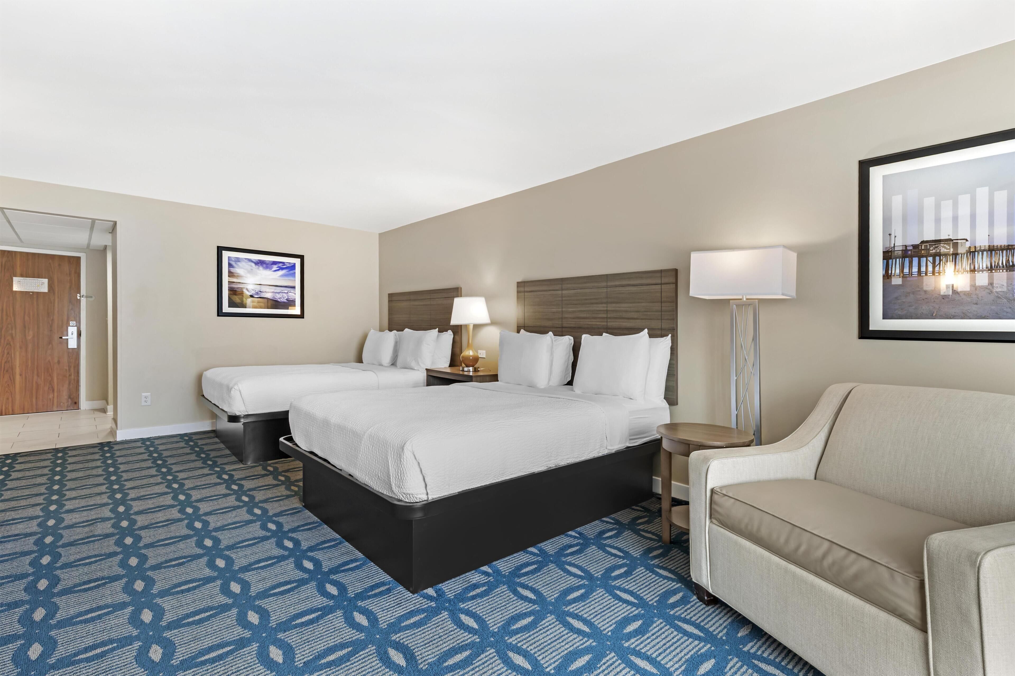 A hotel room with a bed, two bedside tables, a lamp, a couch, and a patterned carpet.