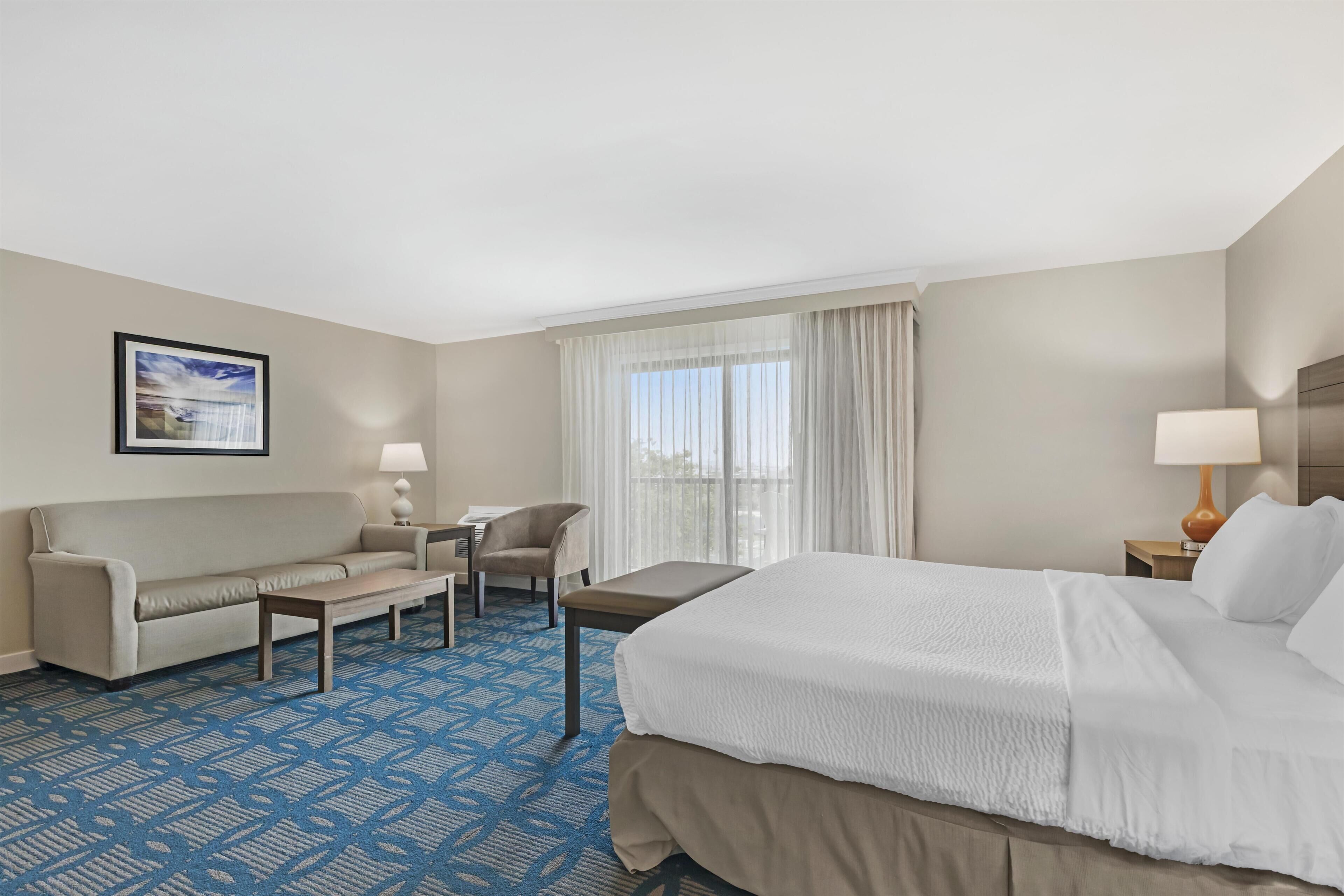 Een hotelkamer met een bed, een slaapbank, een stoel, een klein tafeltje en een raam met gordijnen.