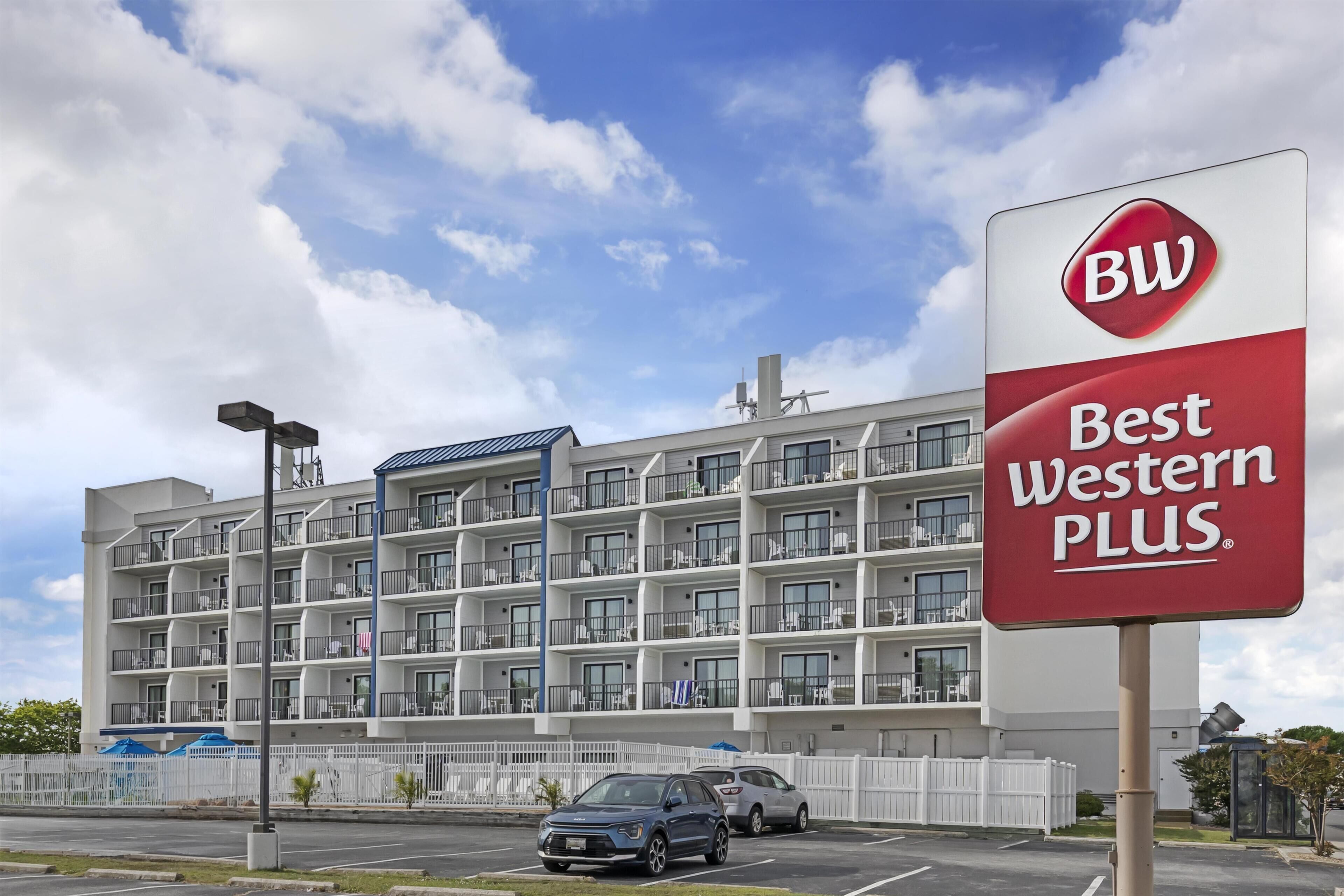 Un edificio de varios pisos con balcones, un letrero de Best Western Plus y un estacionamiento con coches.