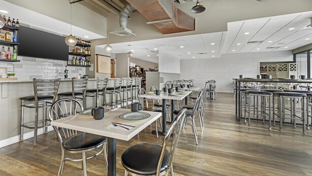 A restaurant with multiple dining tables and chairs, a bar area, and a kitchen in the background. - Best Western Plus Ocean City (Ocean City)