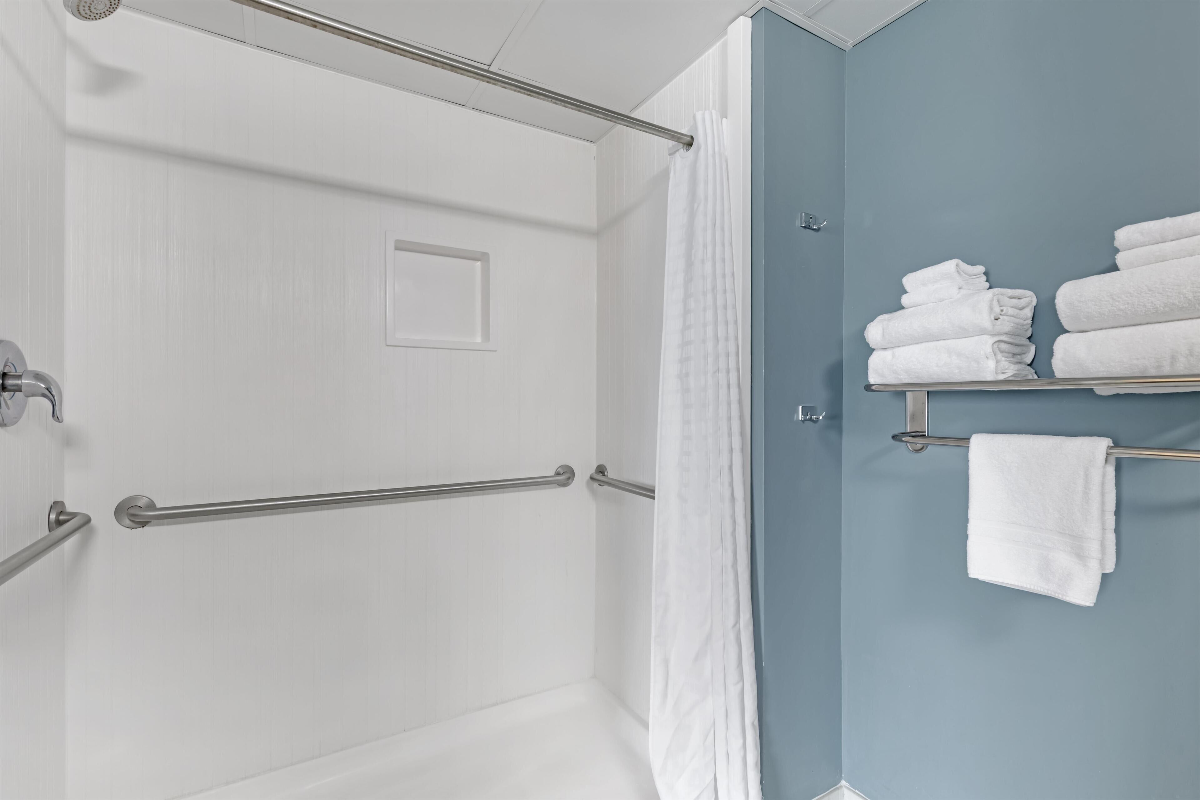 A bathroom with a shower, a towel rack with folded towels, and a door with a handle.