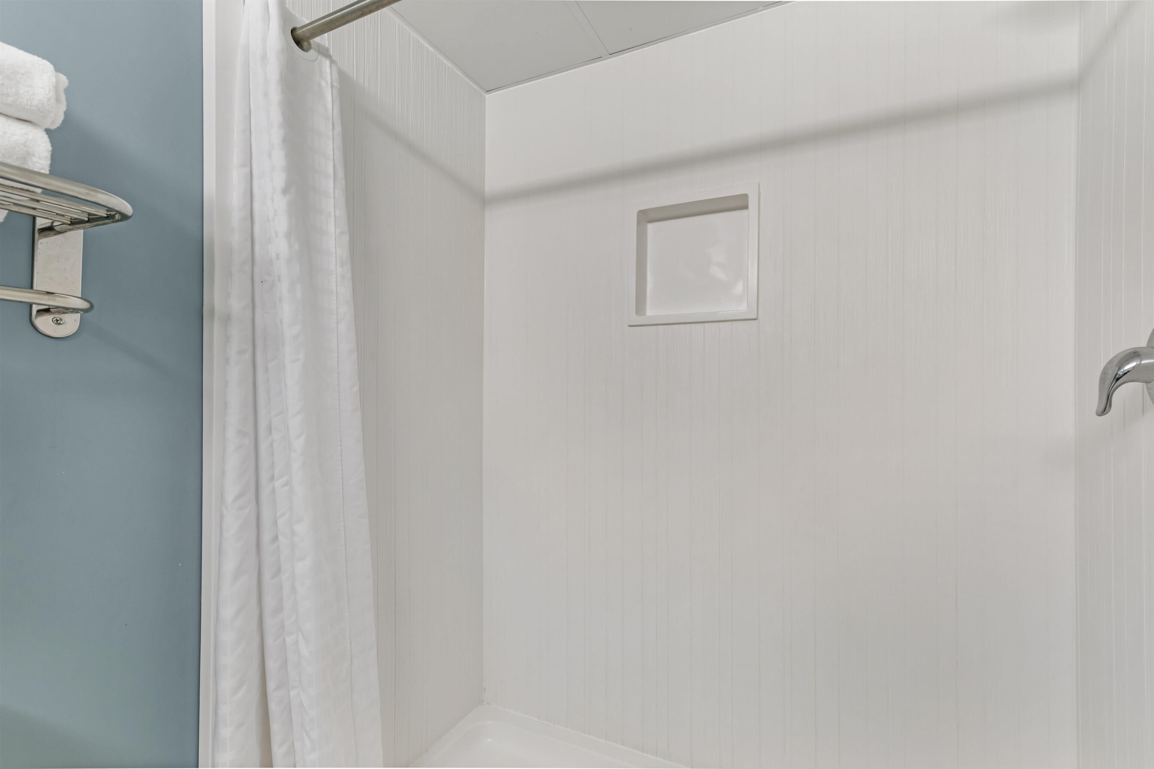 Une salle de bain avec une douche, un porte-serviettes et un petit miroir carré.