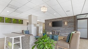 A modern waiting area with a sofa, a coffee table, a TV mounted on a wooden wall, and a potted plant. - Best Western Plus Ocean City (Ocean City)