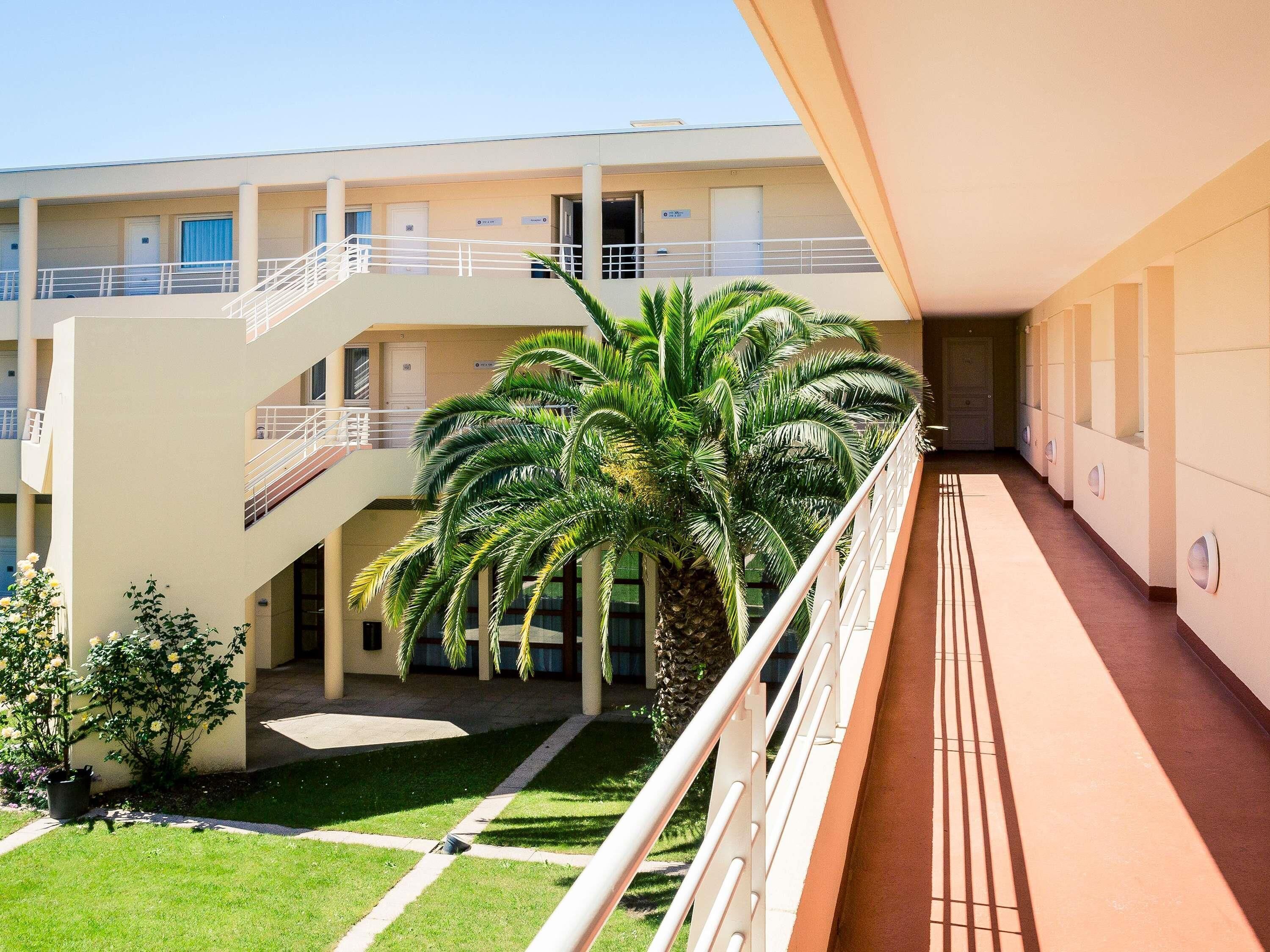 A multi-level hotel with a central courtyard, palm trees, and a balcony with a railing.