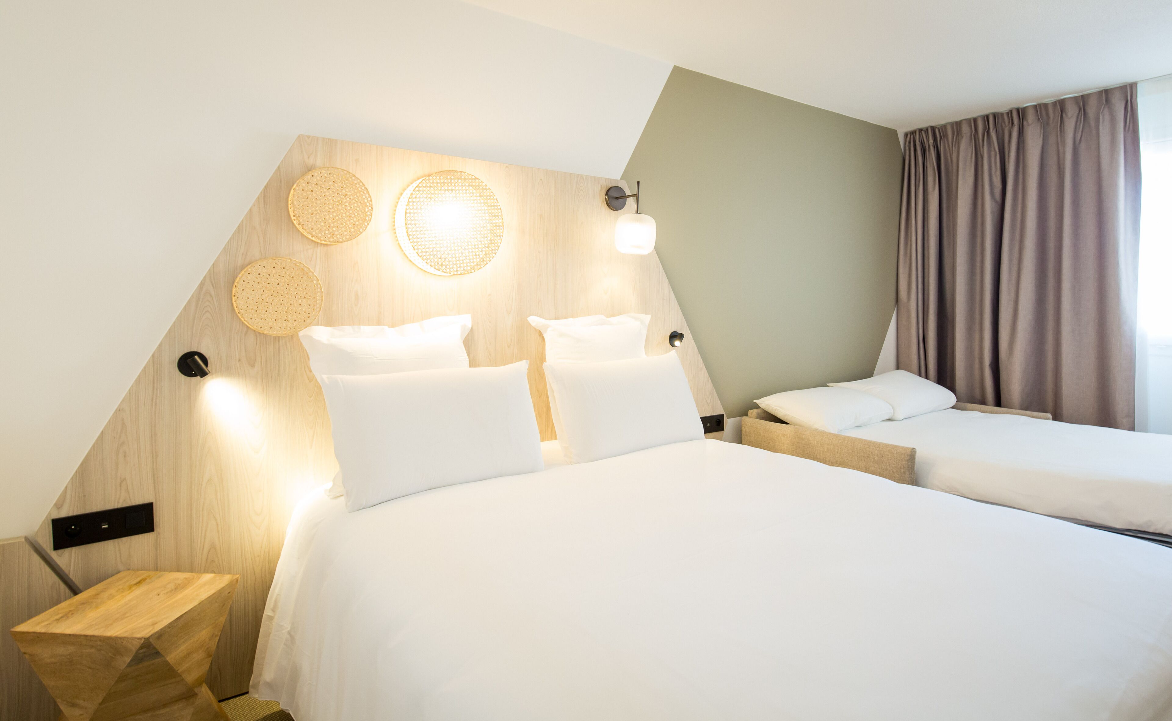 Habitación de hotel con diseño moderno, que incluye una cama grande, una cama más pequeña y un cabecero de madera con luces empotradas.