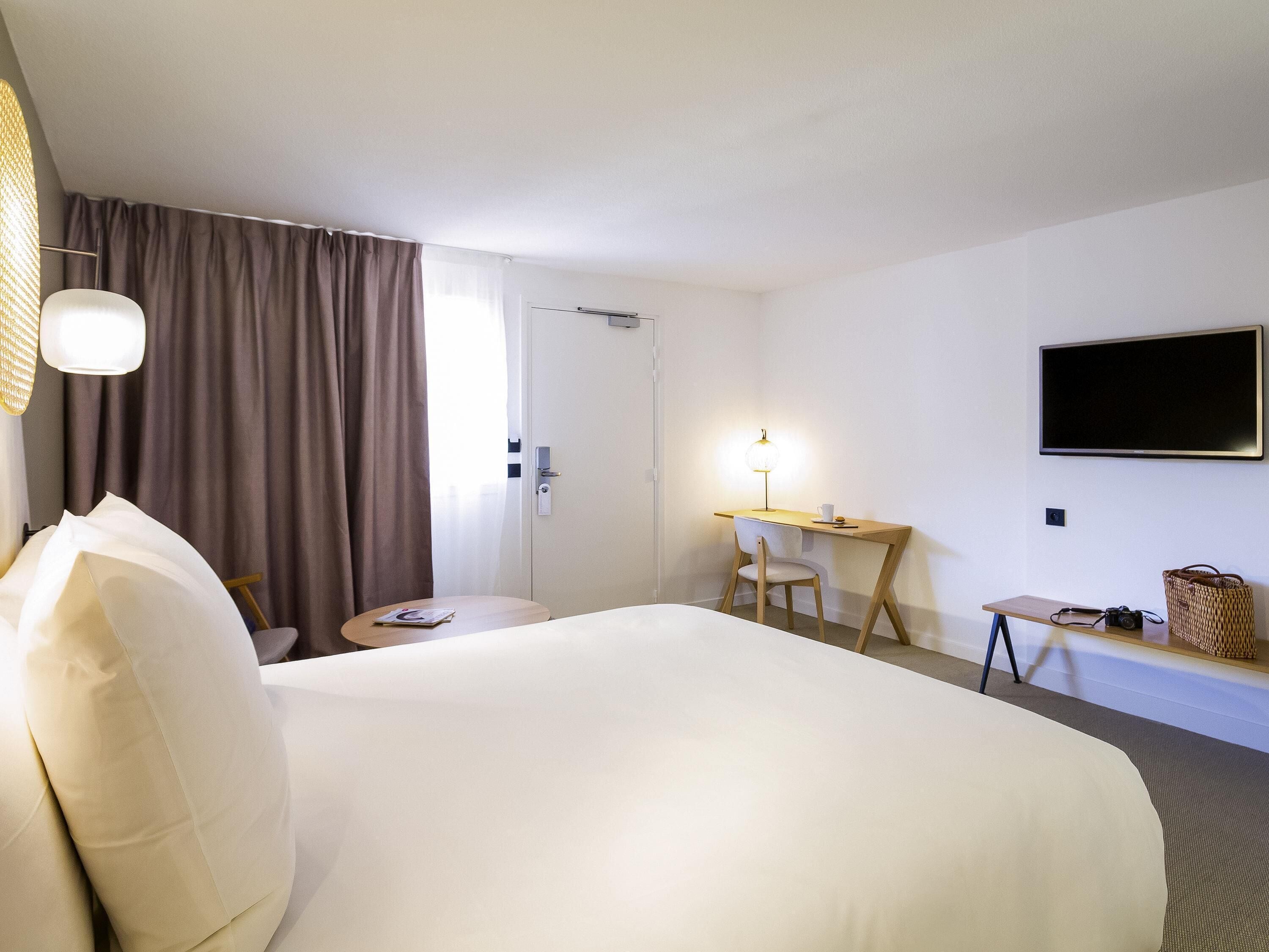A hotel room with a bed, a desk, a chair, a television, and a window with curtains.