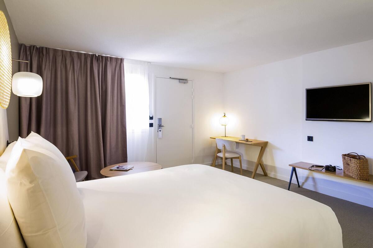 A hotel room with a bed, a desk, a chair, a television, and a window with curtains.