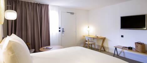 Una habitación de hotel con una cama, un escritorio, una silla, un televisor y una ventana con cortinas.